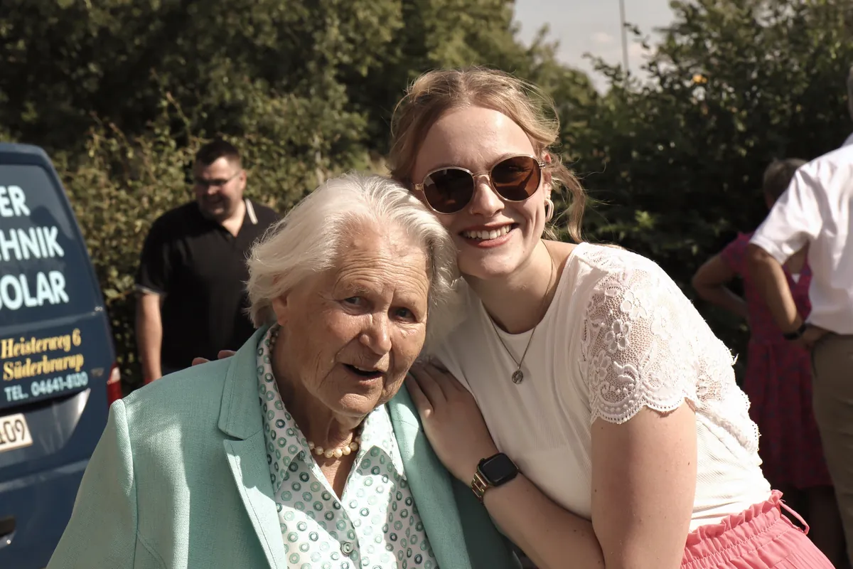 Emma lachend Wange an Wange mit einer älteren Dame bei einer Feier